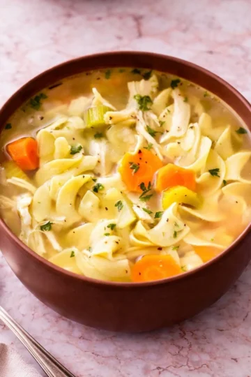 Homemade chicken noodle soup in a bowl with fresh herbs and vegetables