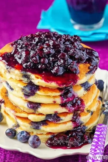 Stack of fluffy blueberry pancakes topped with fresh blueberries and syrup