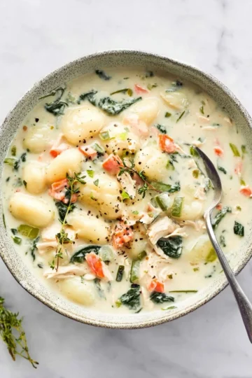 Bowl of delicious Chicken Gnocchi Soup garnished with fresh herbs.