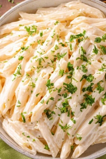 Creamy white sauce penne pasta dish garnished with herbs and cheese.